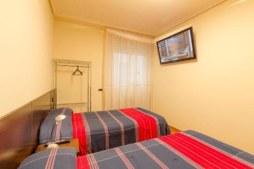A cozy hotel room features two neatly made beds with striped bedding, a mounted TV, and a simple wardrobe, ideal for travelers seeking comfort in a budget-friendly accommodation.