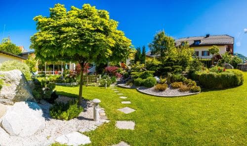 A serene suburban garden with lush greenery, stone pathways, and vibrant flowers under a clear blue sky, ideal for relaxing getaways and nature-inspired travel photography.