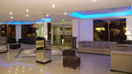 A modern hotel lobby features sleek furniture, reflective floors, and ambient blue lighting, creating a welcoming atmosphere ideal for travelers seeking comfort and style.