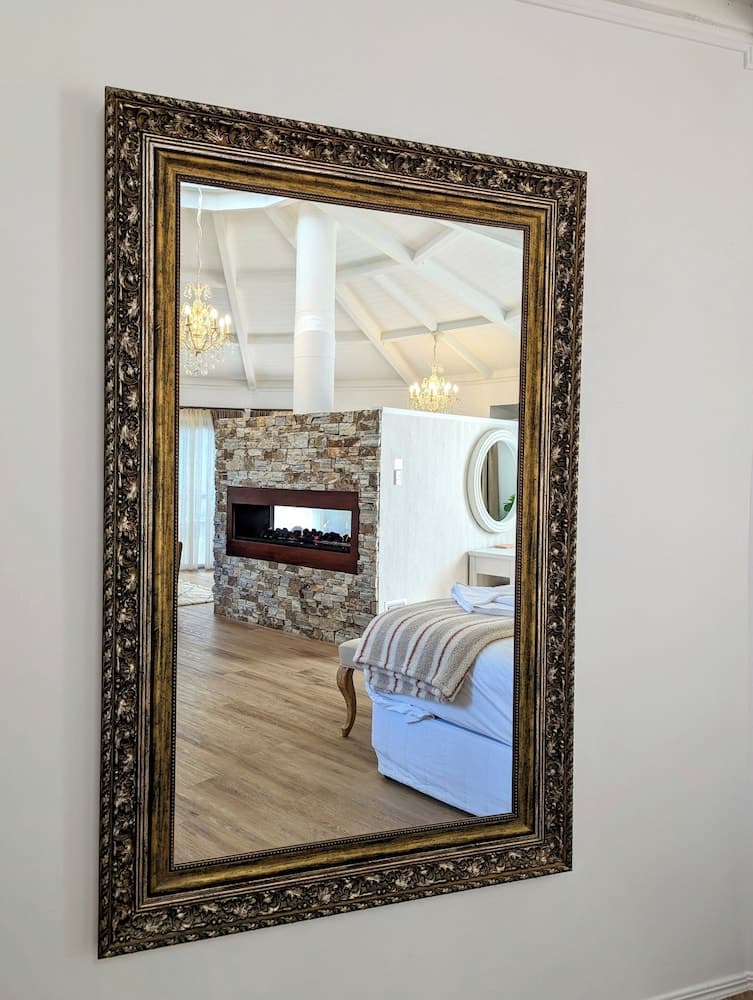A luxurious bedroom scene is reflected in an ornate mirror, showcasing a cozy bed with striped bedding, a stone fireplace, wooden flooring, and elegant chandeliers, ideal for travelers seeking upscale accommodation inspiration.