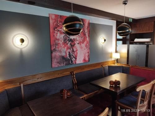A cozy café interior features wooden tables, plush seating, modern spherical pendant lights, and vibrant wall art, creating an inviting atmosphere perfect for travelers seeking a relaxing spot to unwind or work.