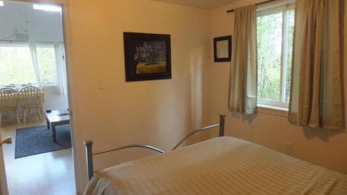 A cozy bedroom with a neatly made bed, framed artwork, and a window offering a serene view of greenery, ideal for travelers seeking a peaceful retreat in a vacation rental.