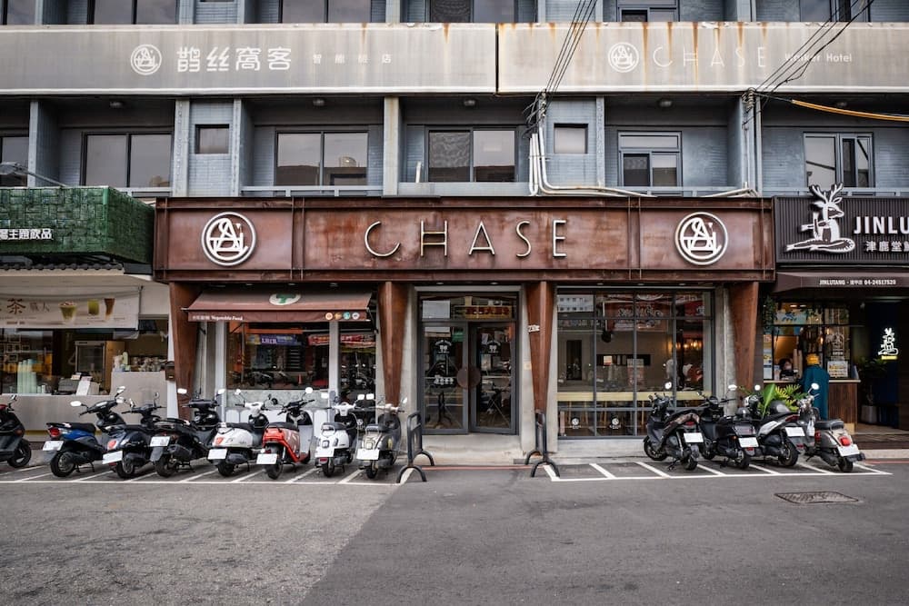 A bustling urban street scene features the rustic facade of a "CHASE" establishment with parked scooters in front, ideal for travelers exploring city nightlife and local dining spots.