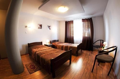 A cozy hotel room with wooden floors, two neatly made beds, warm curtains, and a comfortable chair, ideal for travelers seeking a relaxing stay in a quaint setting.