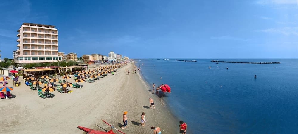 A vibrant beach scene with colorful umbrellas and lounge chairs stretches along the sandy shore under a clear blue sky, ideal for travelers seeking relaxation and coastal activities near a bustling seaside town.