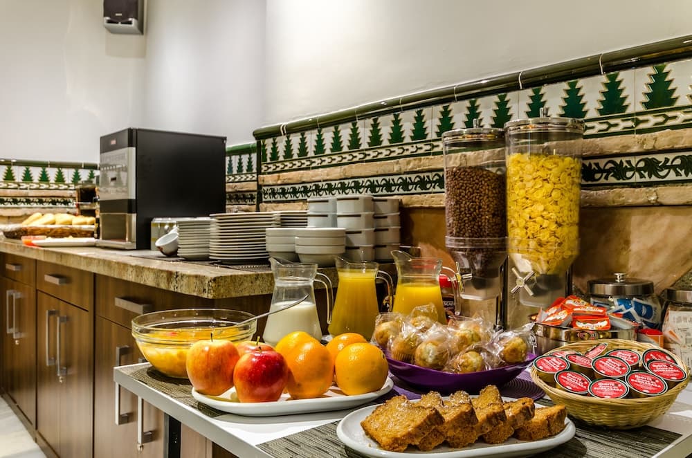 A cozy breakfast buffet area features vibrant fruits, pastries, and cereals against a backdrop of decorative tiled walls, ideal for travelers seeking a warm and inviting start to their day.