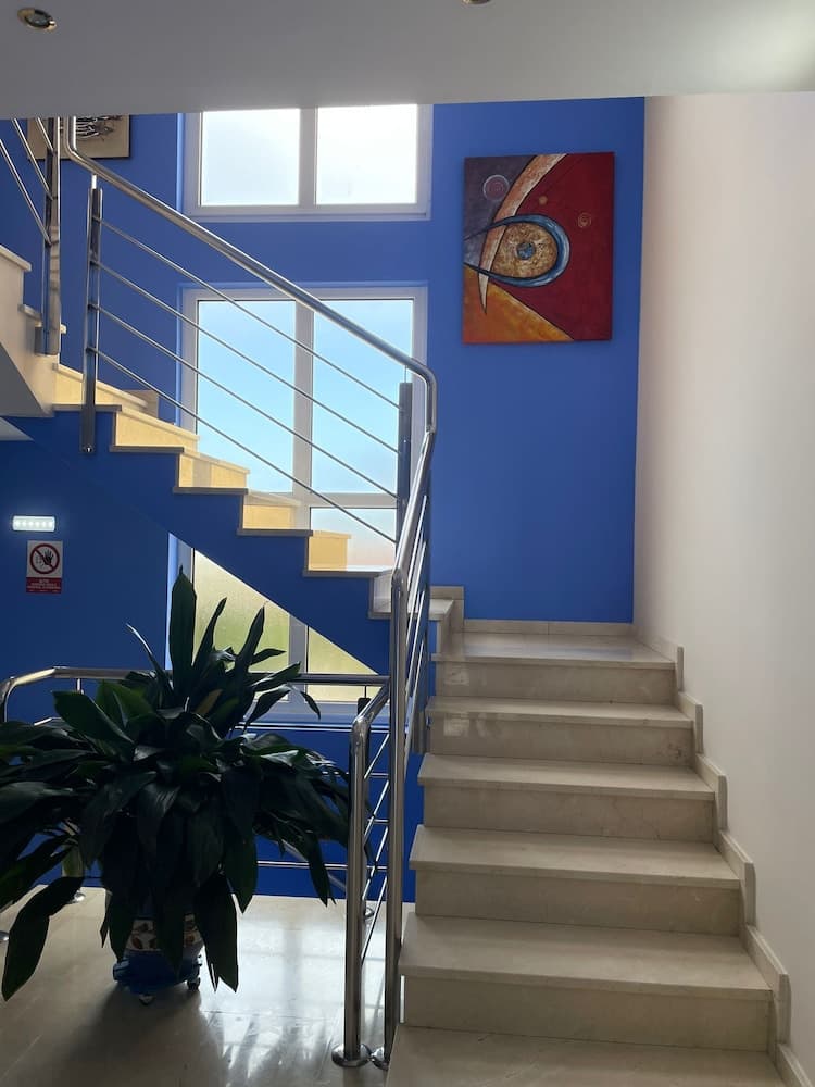 A modern staircase with sleek metal railings ascends against a vibrant blue wall adorned with abstract art, creating an inviting and stylish atmosphere ideal for boutique hotel or contemporary office interior design inspiration.
