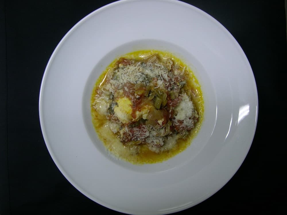 A beautifully plated dish featuring creamy polenta topped with vegetables and grated cheese on a white plate against a dark background, perfect for culinary enthusiasts exploring gourmet dining experiences.