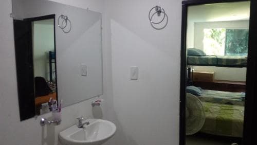 A cozy hotel bathroom with a white sink, mirror, and towel rings reflects a serene bedroom with green bedding, ideal for travelers seeking comfort in compact accommodations.