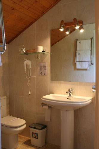 A cozy attic bathroom with wooden ceiling, beige tiled walls, a pedestal sink, and warm lighting creates an inviting atmosphere, ideal for travelers seeking comfort in compact spaces.