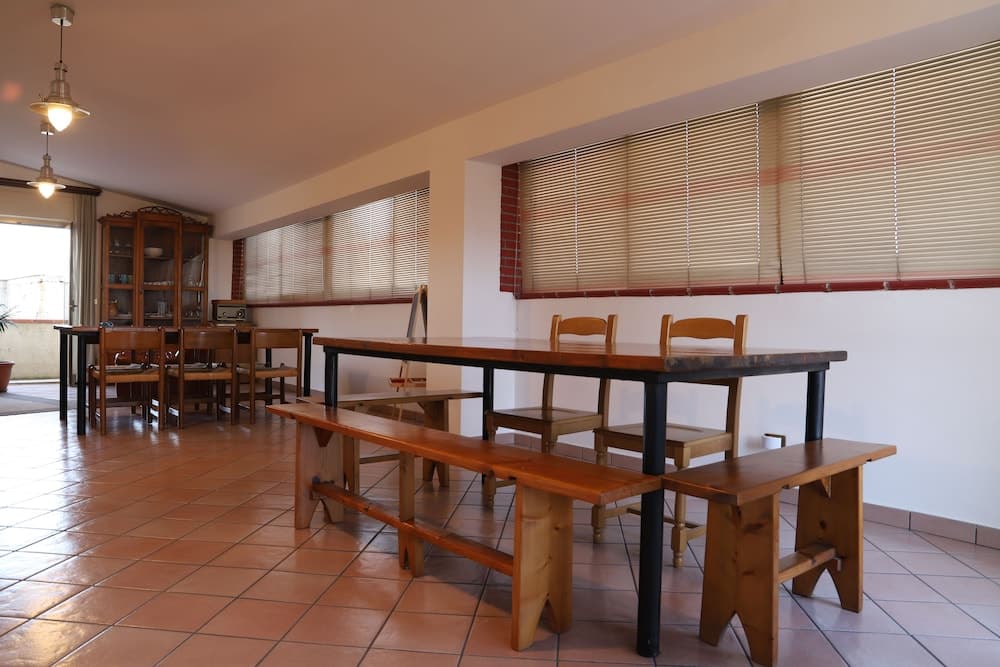 A cozy dining area with wooden tables, benches, and chairs under soft lighting, featuring tiled floors and window blinds, ideal for travelers seeking a warm and inviting space for meals or gatherings.