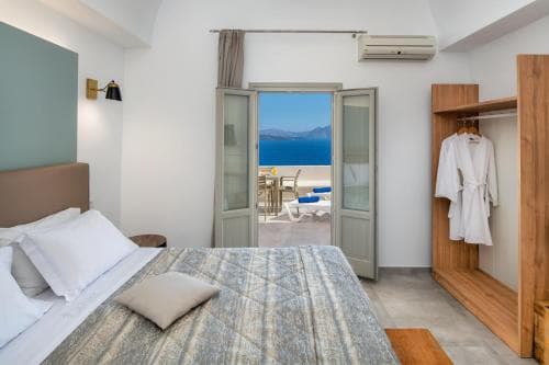 A serene hotel room with a cozy bed, wooden closet, and open doors leading to a balcony overlooking the tranquil sea, perfect for a relaxing seaside getaway.
