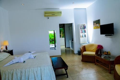 A cozy, well-lit hotel room with a neatly made bed, a comfortable armchair, and a view of lush greenery through an open door, ideal for travelers seeking relaxation and comfort.