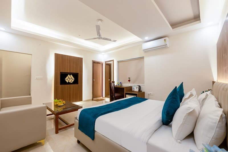 A cozy hotel room in Noida's Industrial Area features a neatly made bed with blue accents, a modern desk setup, and ambient lighting, ideal for travelers seeking comfort and convenience near business hubs.