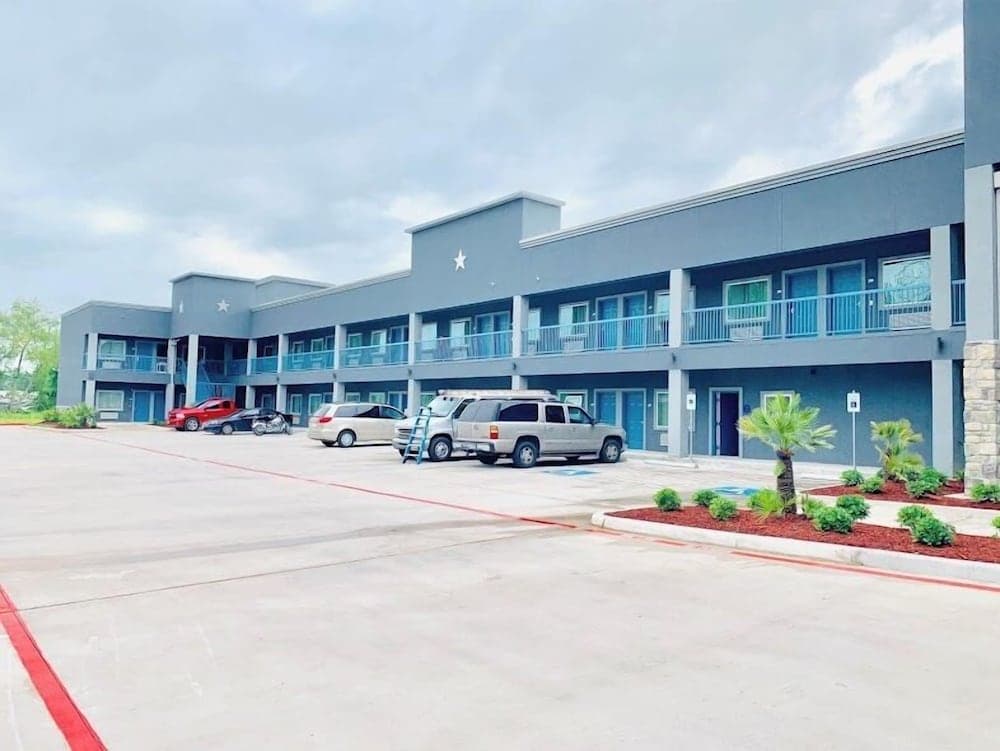 A modern motel with blue balconies and star decorations offers a welcoming atmosphere under a cloudy sky, ideal for travelers seeking convenient lodging with ample parking and landscaped surroundings.
