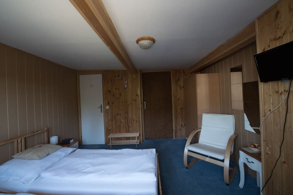 A cozy cabin-style hotel room with wooden paneling, a neatly made bed, a comfortable chair, and a small table creates a serene atmosphere ideal for travelers seeking relaxation in a rustic setting.