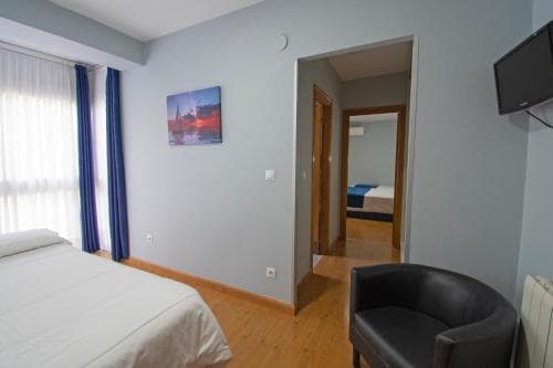 A cozy hotel room features a neatly made bed, a leather armchair, wooden flooring, and a serene sunset painting, creating a calm and inviting atmosphere ideal for travelers seeking relaxation.