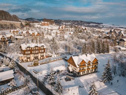 A picturesque winter village scene with snow-covered chalets nestled among pine trees under a serene sky, ideal for a cozy ski resort getaway.