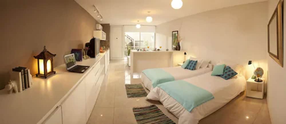 A cozy, well-lit bedroom with twin beds adorned in turquoise bedding, a long countertop featuring a laptop and decorative lantern, and an inviting open-plan layout creates a serene atmosphere ideal for travelers seeking comfort and functionality.