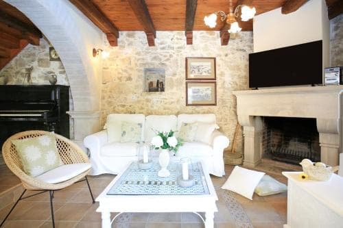 A cozy living room with stone walls, wooden beams, and a fireplace exudes rustic charm, perfect for travelers seeking a warm and inviting retreat in a countryside villa.