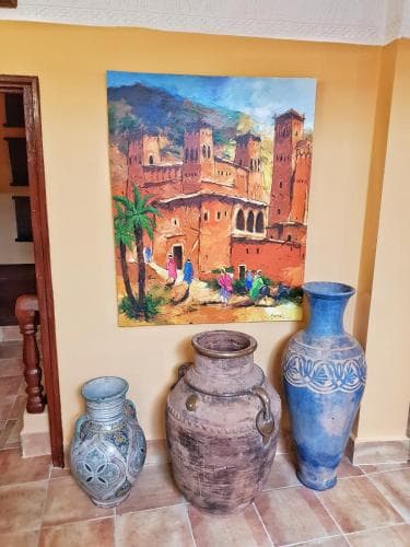 A warmly lit indoor space features a vibrant painting of a desert fortress scene above three ornate ceramic vases, creating an inviting atmosphere ideal for cultural exploration enthusiasts.