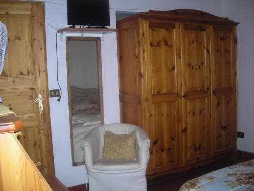 A cozy hotel room features rustic wooden furniture, a comfortable armchair with a cushion, and a mirror reflecting the bed, ideal for travelers seeking a warm and inviting atmosphere.