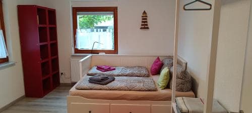 A cozy bedroom with twin beds adorned in patterned bedding, a red shelving unit, and a window view of greenery, ideal for travelers seeking a comfortable and serene accommodation.