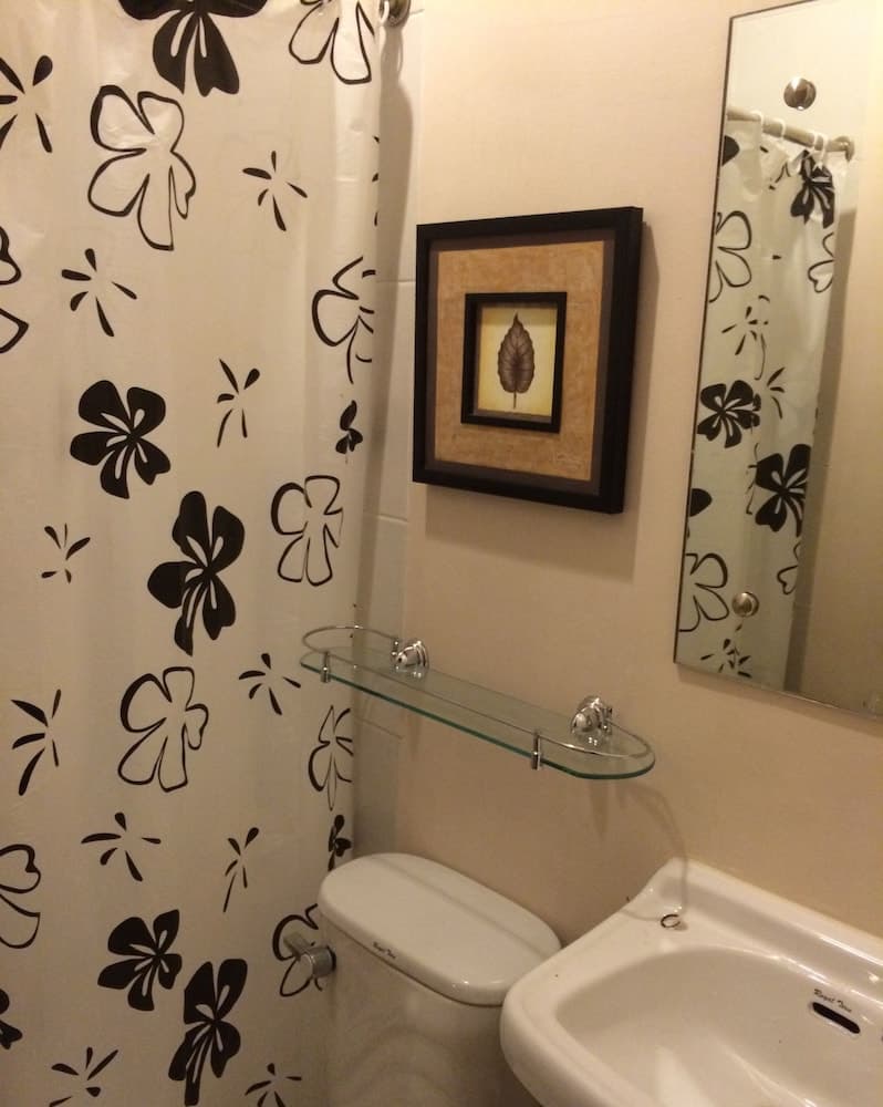 A cozy bathroom features a black-and-white floral shower curtain, a framed leaf artwork, and a glass shelf, creating an inviting and stylish space ideal for travelers seeking comfort and charm.