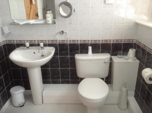 A compact bathroom with white fixtures, tiled walls, and essential toiletries creates a clean and functional space ideal for travelers seeking basic amenities.