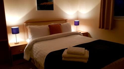 A cozy hotel room features a neatly made bed with soft lighting from blue lamps, creating a warm and inviting atmosphere ideal for travelers seeking relaxation.