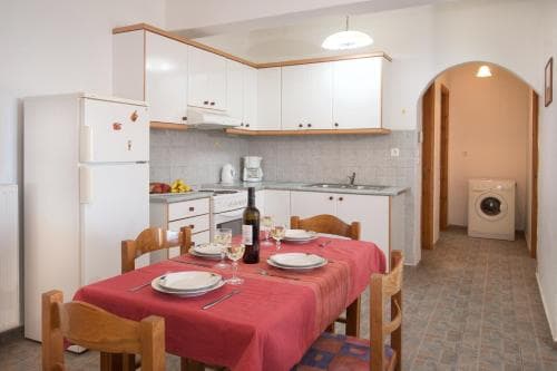 A cozy apartment kitchen with white cabinetry, a red tablecloth-covered dining area, and a visible laundry room, ideal for travelers seeking self-catering accommodations in a warm and inviting setting.