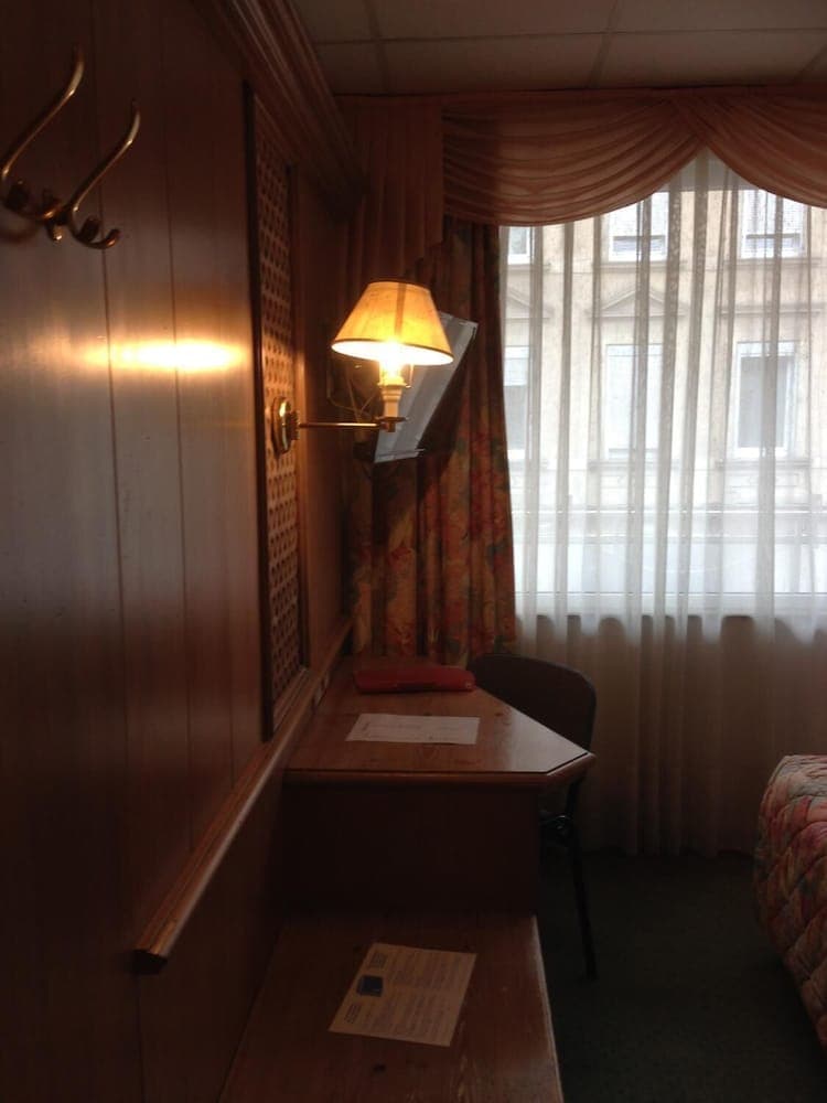 A cozy hotel room corner features a wooden desk with a warm lamp, patterned curtains, and a view of urban architecture, ideal for travelers seeking a quiet work or relaxation space.
