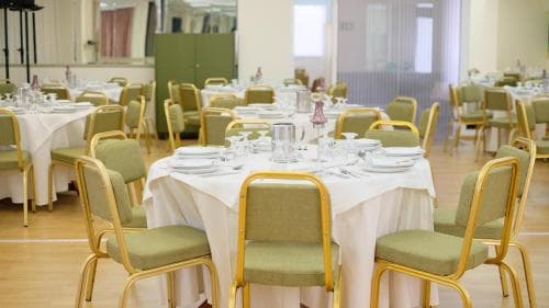 A cozy indoor dining area with neatly arranged tables covered in white linens, green chairs, and elegant tableware, evokes a welcoming atmosphere ideal for group gatherings or corporate events.