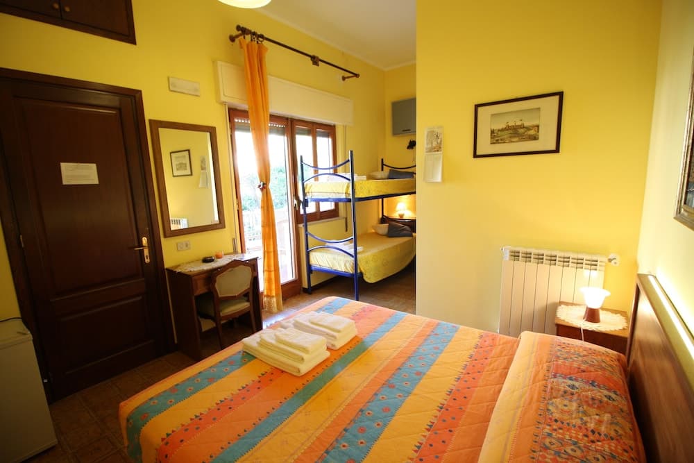 A cozy, warmly-lit hotel room features vibrant yellow walls, a colorful bedspread, bunk beds, and a view of greenery through glass doors, ideal for travelers seeking comfort and charm.