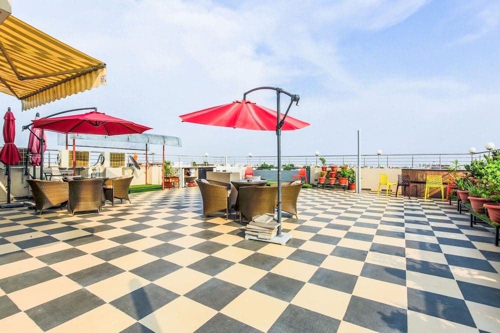A vibrant rooftop terrace with a checkered floor, colorful umbrellas, and cozy seating offers a relaxing urban retreat perfect for travelers seeking a scenic spot to unwind.