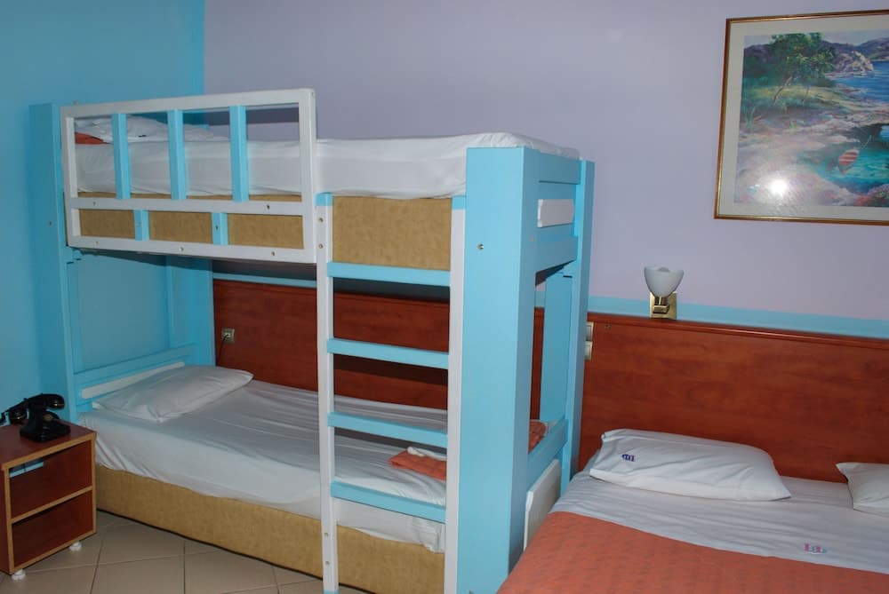 A cozy hotel room features blue bunk beds, a single bed with wooden headboard, and a serene wall painting, ideal for family travelers seeking comfortable accommodations.