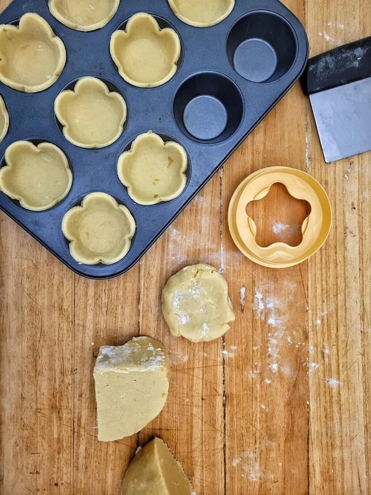 A cozy kitchen scene featuring a muffin tin filled with flower-shaped dough cups, a star cookie cutter, and pastry tools on a wooden surface, perfect for culinary enthusiasts seeking creative baking ideas.