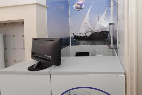 A serene reception area features a computer on a white desk against a backdrop of a traditional sailing ship mural, ideal for travelers seeking a calm and culturally rich check-in experience.