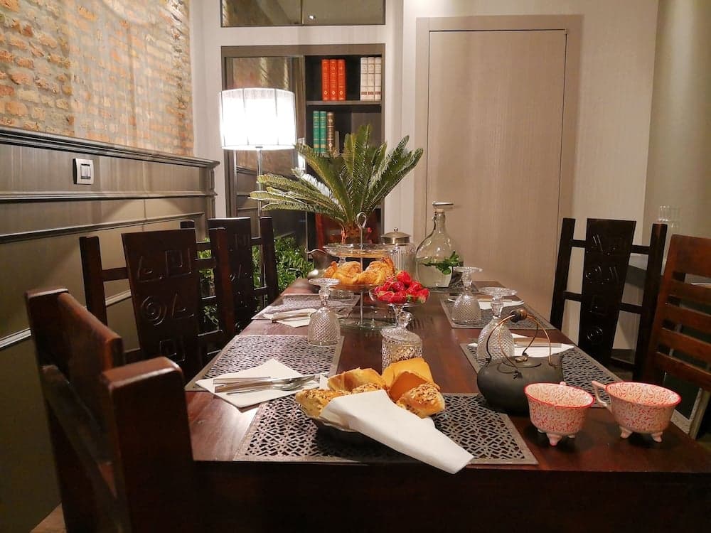 A cozy dining room with a rustic brick wall, wooden table set with bread, strawberries, and decorative cups, exudes warmth and charm, perfect for travelers seeking an intimate and inviting meal setting.