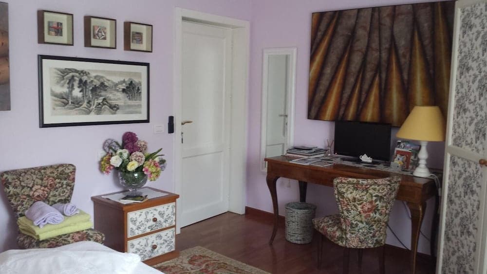 A cozy bedroom with lavender walls, floral-patterned furniture, and a wooden desk adorned with books and a lamp, ideal for travelers seeking a serene and artistic retreat.
