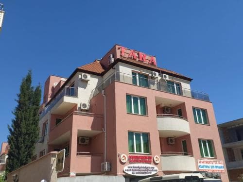 A vibrant pink hotel with balconies and a bold "ARA" sign stands under a clear blue sky, offering travelers a cozy urban retreat with convenient amenities.