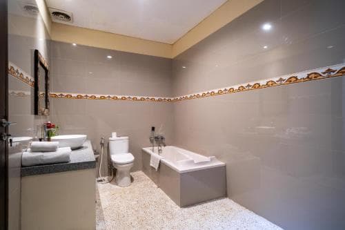 A modern bathroom with beige walls, a bathtub, sink, toilet, and decorative border offers a clean and cozy atmosphere ideal for travelers seeking comfort during their stay.