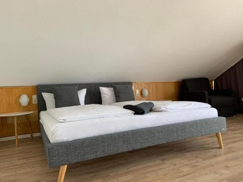 A cozy attic bedroom with a modern gray bed, wooden flooring, and minimalist decor offers a serene retreat for travelers seeking a quiet stay.