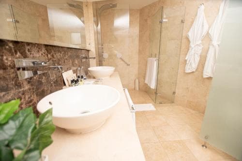 A luxurious hotel bathroom features a modern sink, glass shower enclosure, plush towels, and a serene ambiance, ideal for travelers seeking comfort and relaxation.
