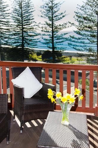 A cozy balcony with wicker furniture and vibrant yellow flowers overlooks lush pine trees and distant mountains, creating a serene retreat ideal for relaxation during a nature-focused getaway.