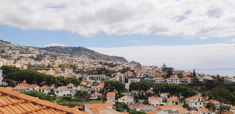 A picturesque coastal town with terracotta-roofed houses nestled among lush greenery under a partly cloudy sky, ideal for travelers seeking serene hillside views and cultural exploration.