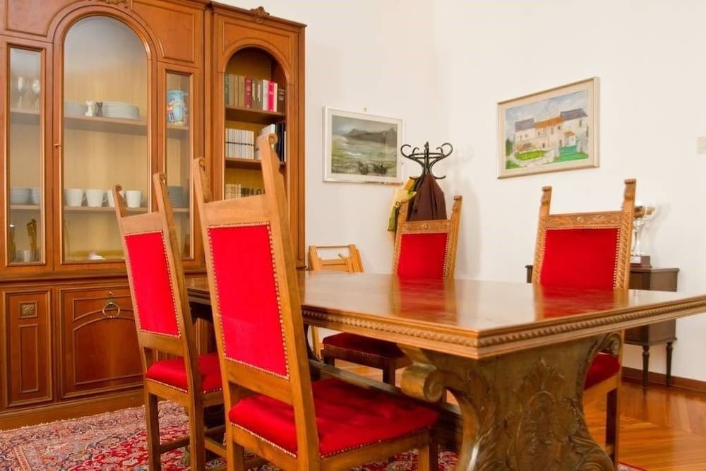 A cozy dining room features a polished wooden table surrounded by red-cushioned chairs, a glass-fronted cabinet filled with dishes, and wall-mounted paintings, ideal for travelers seeking a charming and inviting accommodation setting.