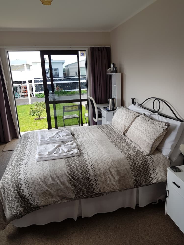 A cozy bedroom with neatly arranged bedding and towels opens to a serene garden view through sliding glass doors, ideal for travelers seeking comfort and relaxation in a vacation rental.