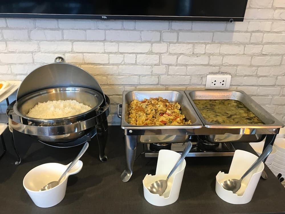 A cozy hotel buffet setup features steaming trays of rice, scrambled eggs, and soup against a white brick wall, perfect for travelers seeking a convenient and warm breakfast experience.