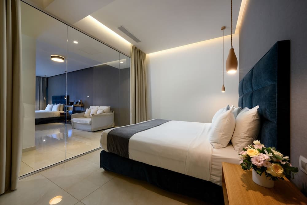 A modern hotel bedroom with sleek furnishings, a cozy bed adorned with plush pillows, a vase of fresh flowers on the bedside table, and a mirrored wall reflecting the serene ambiance, ideal for travelers seeking comfort and style.